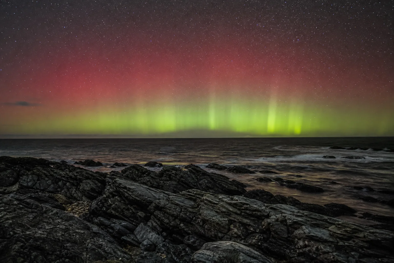 An AI-created southern aurora glowing above a rocky ocean coast